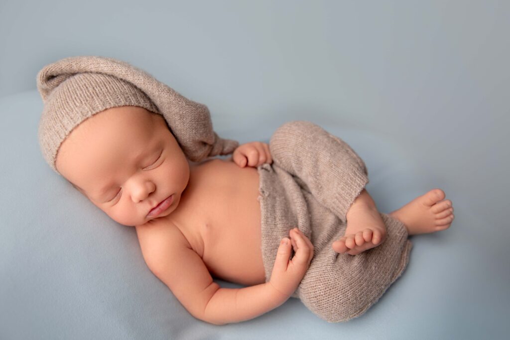 Sleeping baby boy in knit bonnet on blue backdrop during Phoenix in-studio newborn photography session.