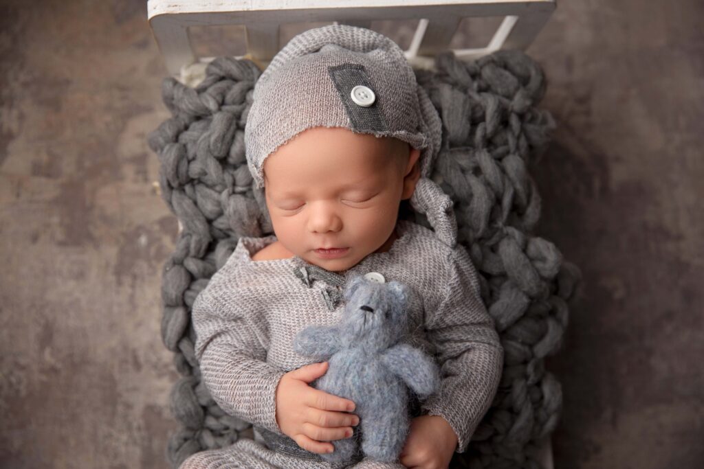 Newborn baby boy holding blue teddy bear during luxury Phoenix newborn photography session.