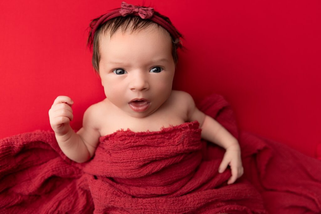 Awake newborn baby wrapped in crimson fabric at Phoenix newborn photography studio.