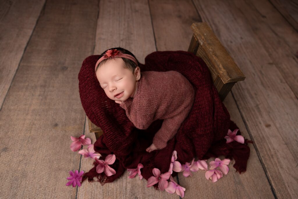 Sleeping newborn baby girl posed on rustic wooden bed in Phoenix photography studio.