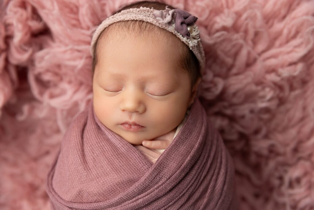 Close-up portrait of a sleeping newborn baby girl wrapped in a purple knit with a delicate headband during a Phoenix newborn photography session. This detailed image highlights the fine art style of a Phoenix newborn photographer.