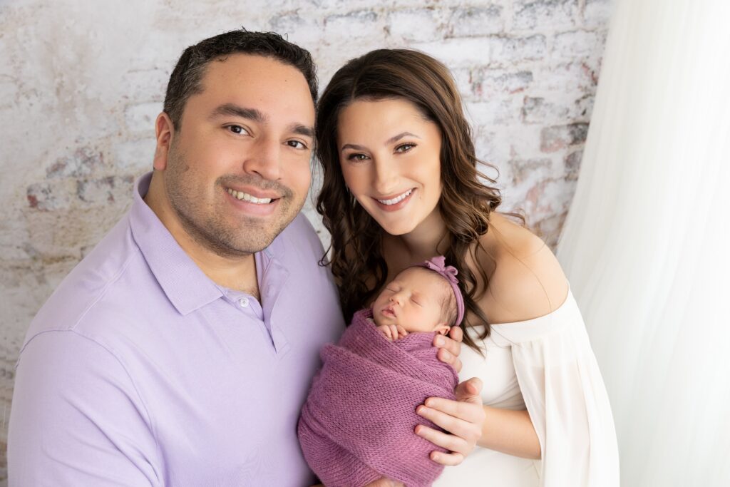 Parents holding their newborn baby during a Phoenix newborn photography session in a bright studio setting. Family portraits are an important part of Phoenix newborn photography experiences.