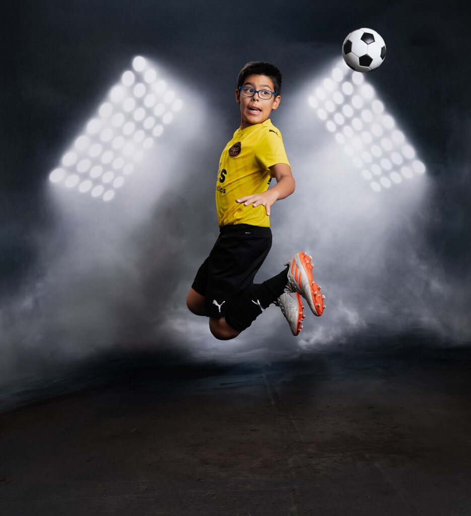 Youth soccer player jumping toward a ball in a dramatic Phoenix studio action sports portrait.