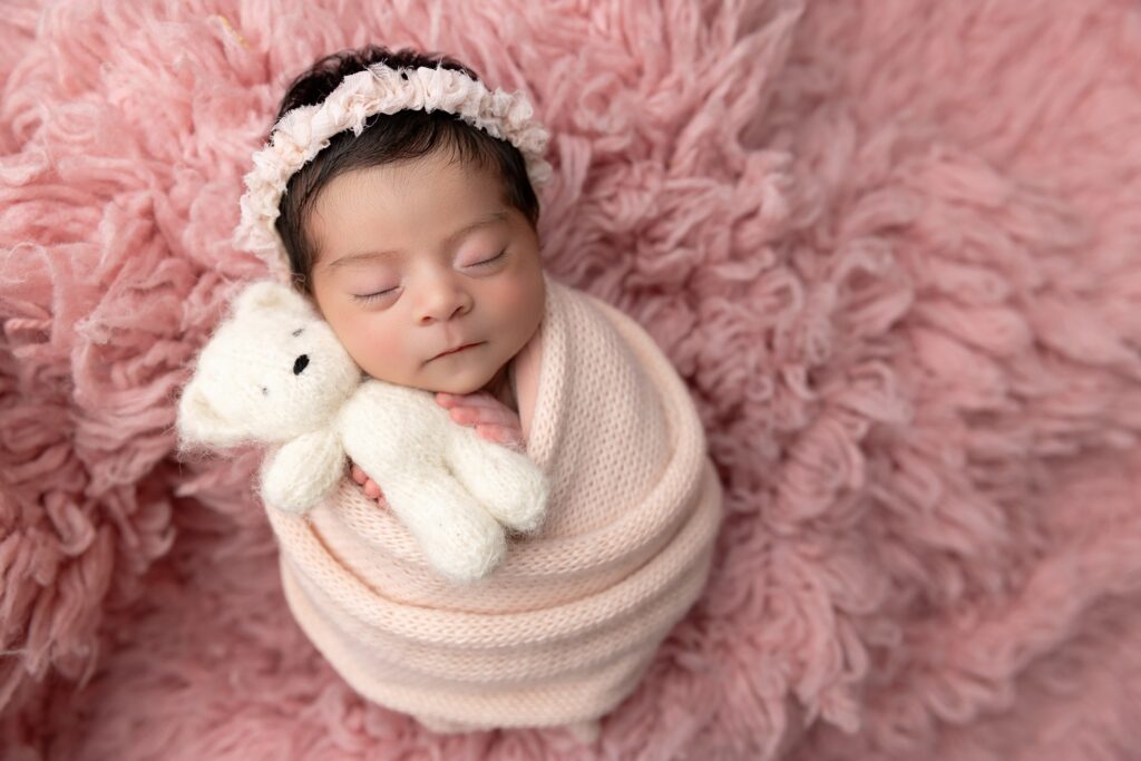 Sleeping newborn girl wrapped in blush knit holding teddy bear at Phoenix newborn photography studio.