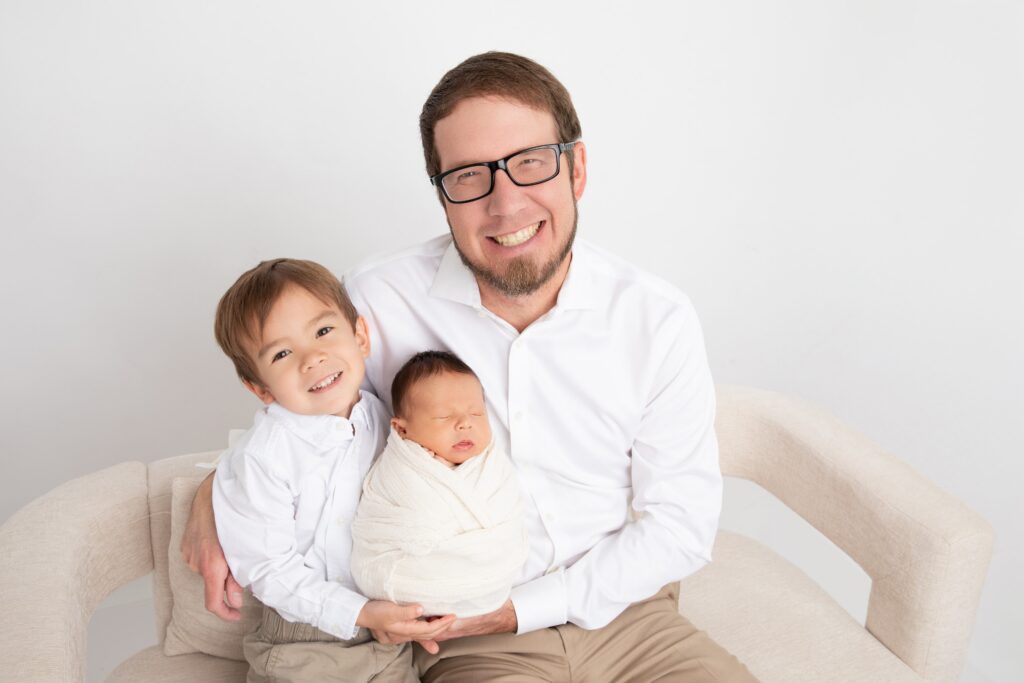 Dad and toddler boy holding their newborn baby brother during an in-studio newborn photography session.
