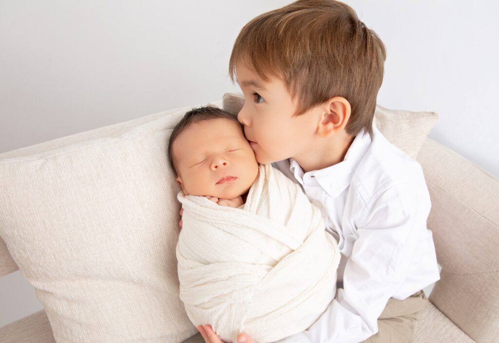 In-studio newborn family portrait showing siblings bonding with their newborn baby brother.